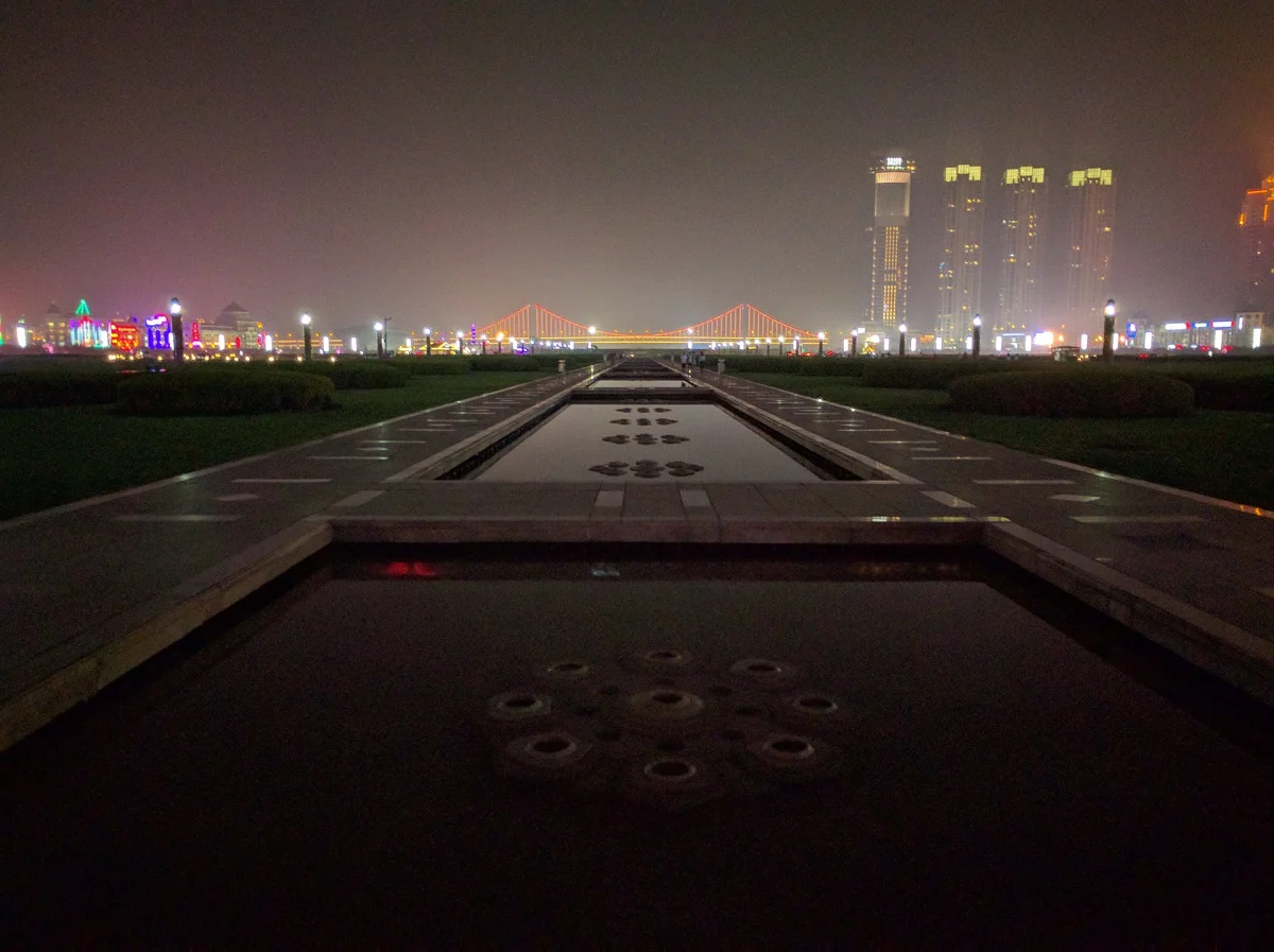 Xinghai Square fountain axis and distant skyline lights at night