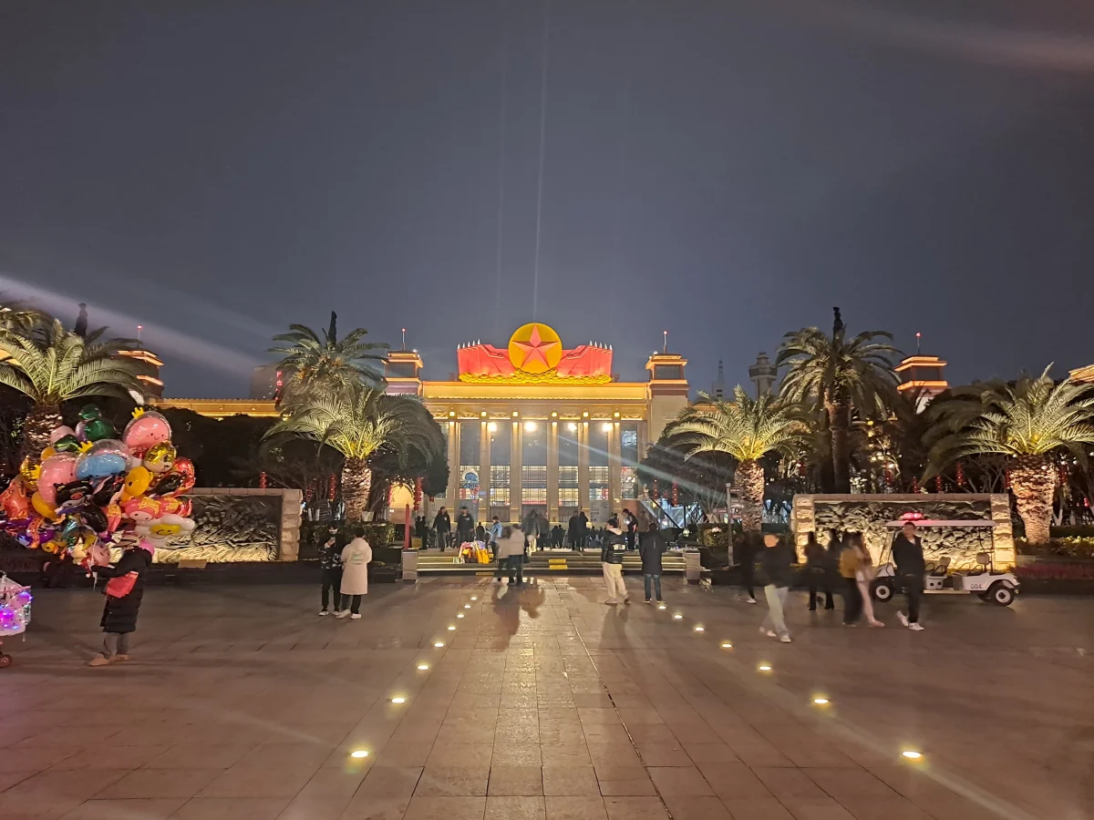 People walking through the front plaza of Bayi Square in Nanchang at night