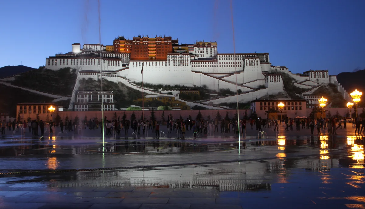 Potala Palace lit at night with plaza water reflections