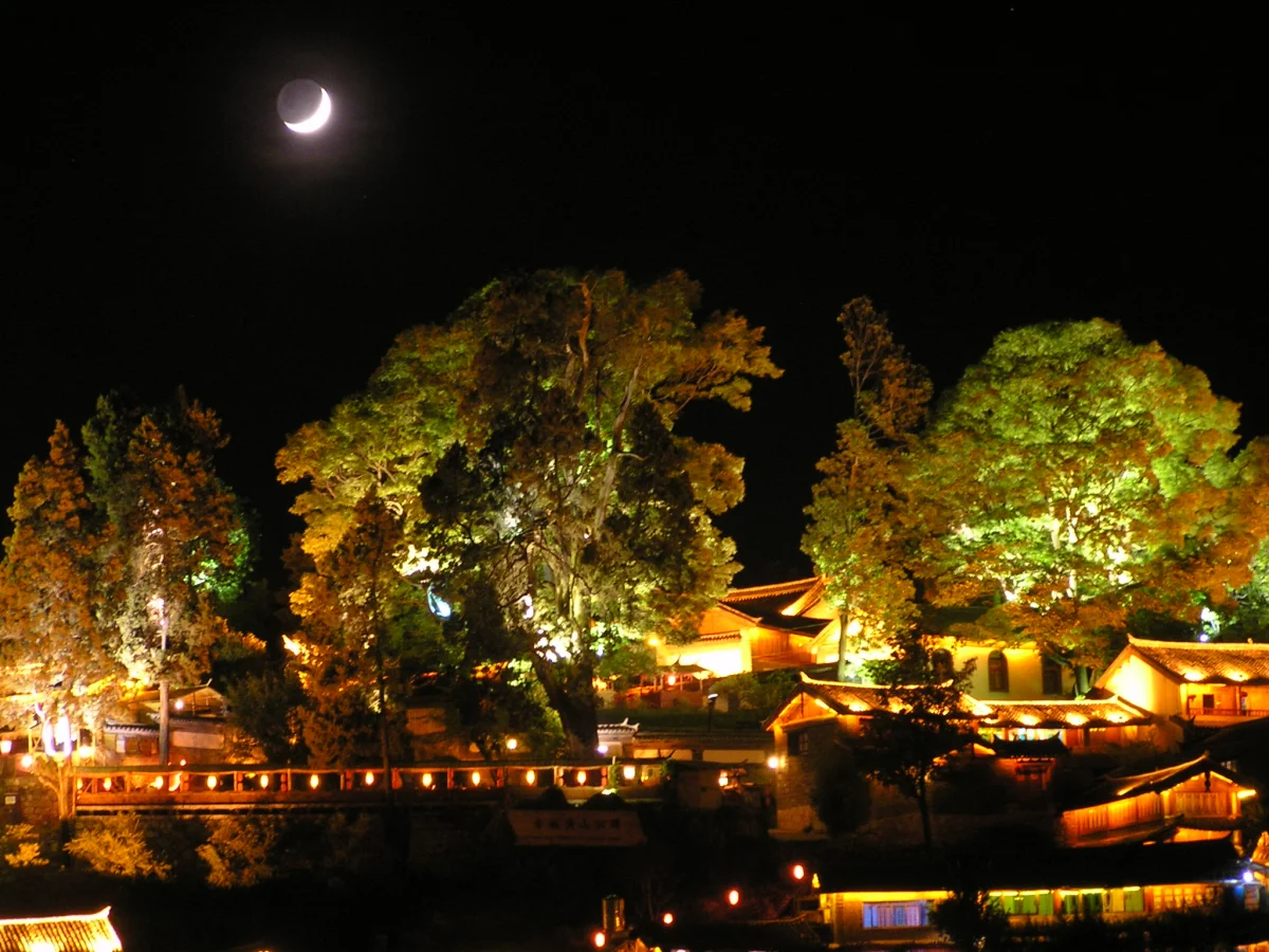 Moon above lit roofs and water in Lijiang Old Town