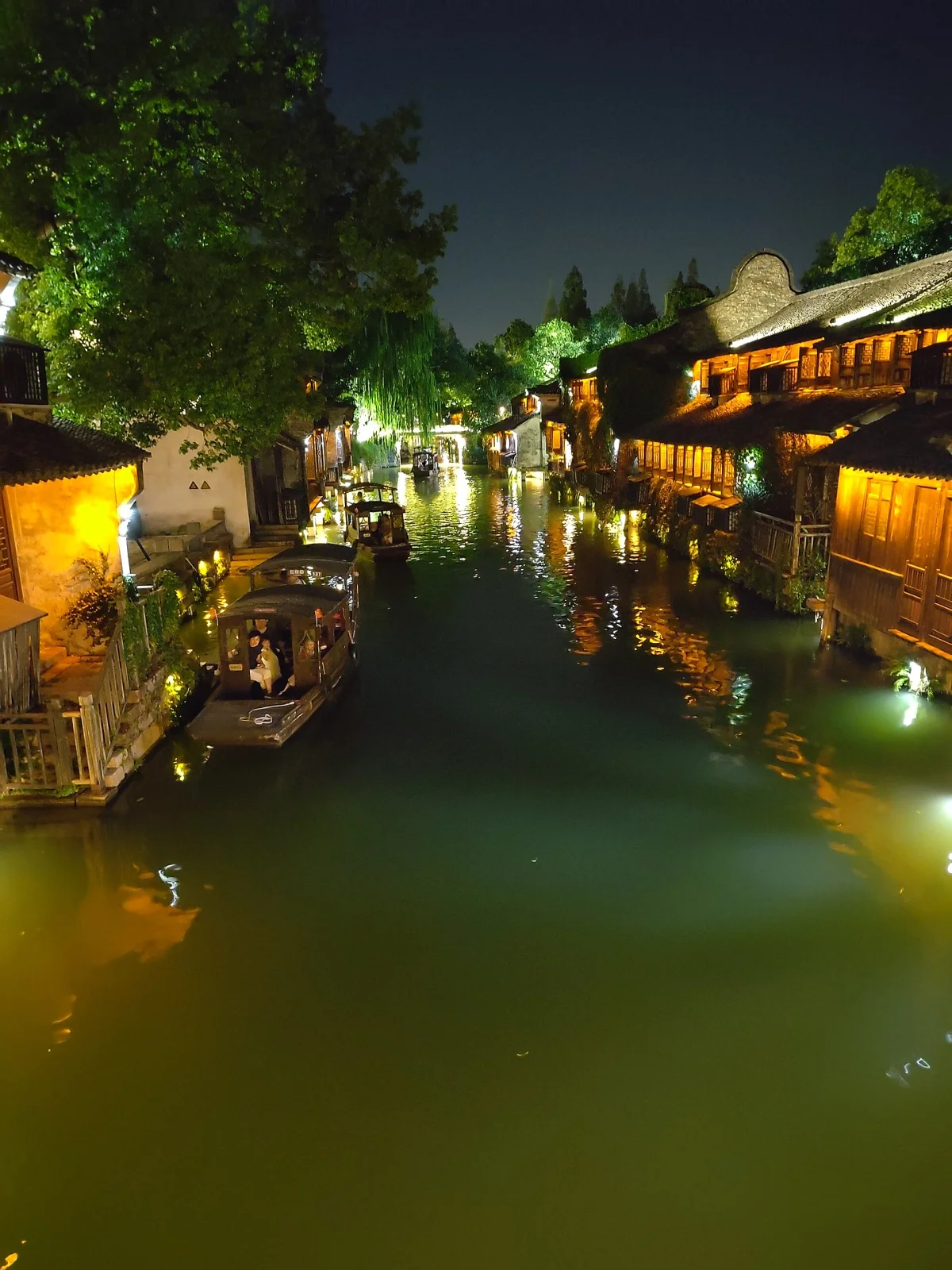 Night boat moving through Wuzhen water-town canal lights
