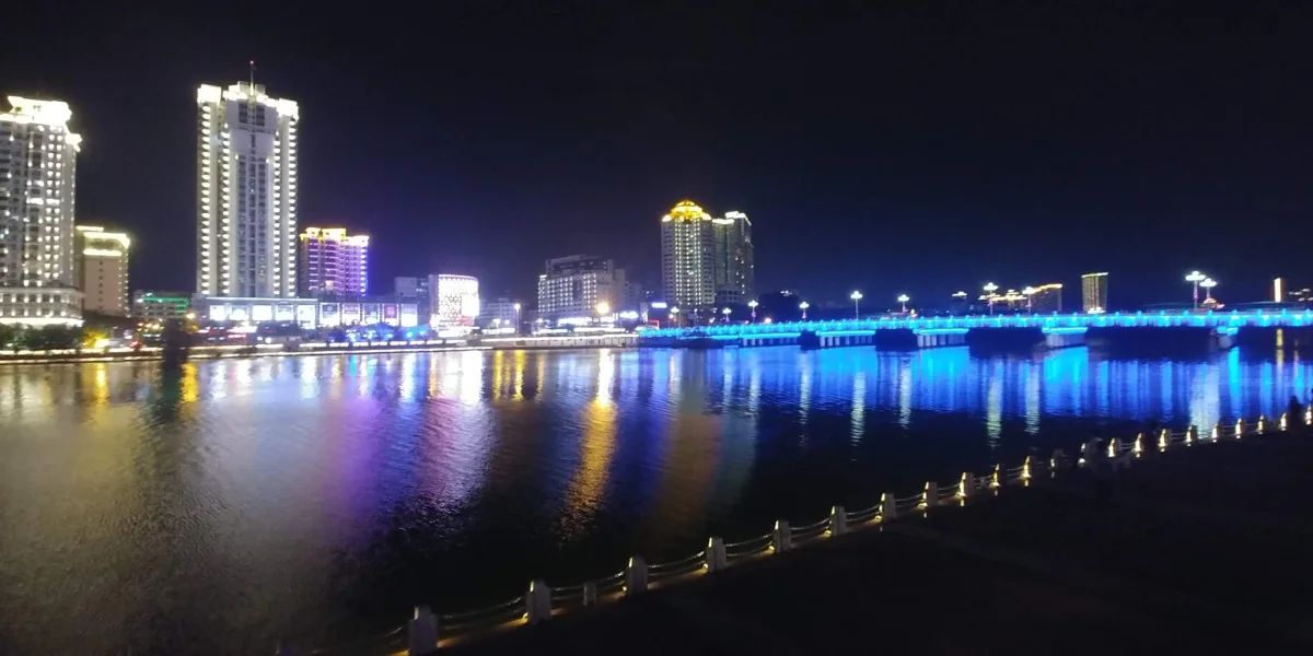 Blue-lit riverside bridge and skyline on the Linchun River at night