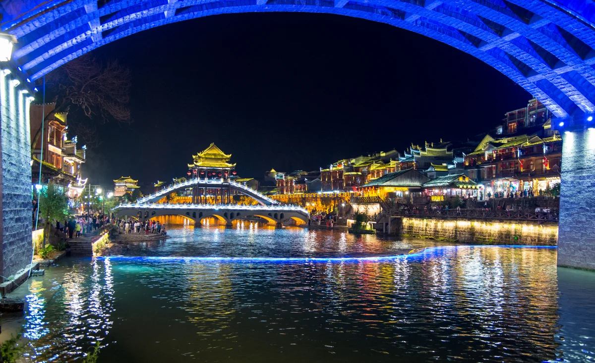 Fenghuang riverfront framed beneath an illuminated bridge